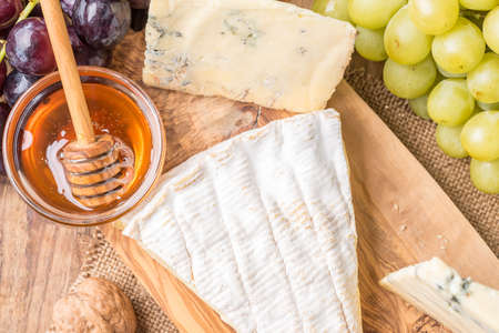 wooden board with cheeses, grapes, nuts and honeyの写真素材