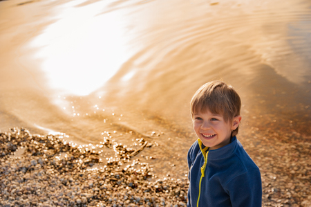 blond child smiles by the lake at sunsetの写真素材