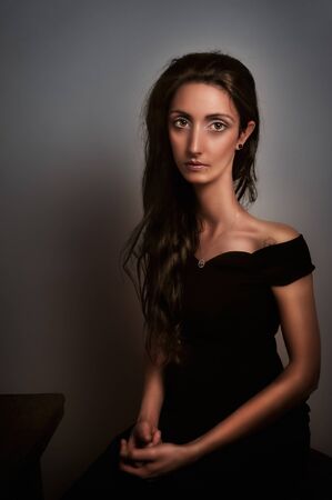 young girl with a long neck in Modigliani style, sitting with arms in her lap in a dark and peaceful atmosphereの写真素材