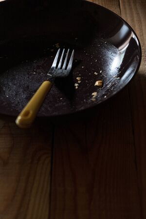 empty plate dirty with crumbs with a yellow fork in a quiet and dark atmosphereの写真素材