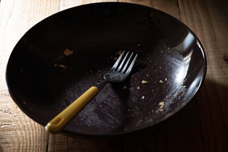 empty plate dirty with crumbs with a yellow fork in a quiet and dark atmosphere