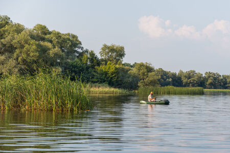 Man fishing at riverside on a little boatの写真素材