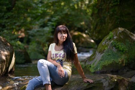 Nice girl posing on a rock in the middle of a little riverの写真素材