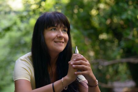 Nice girl smiling and smocking an electronic cigarette in the woodの写真素材