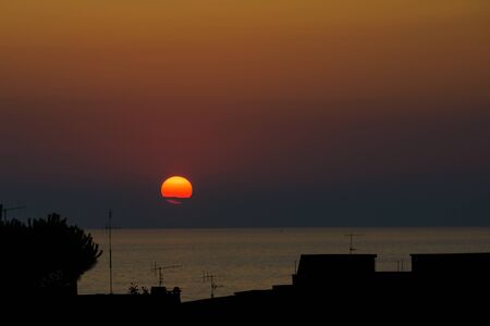 Big round red and orange sun go down in the seaの写真素材