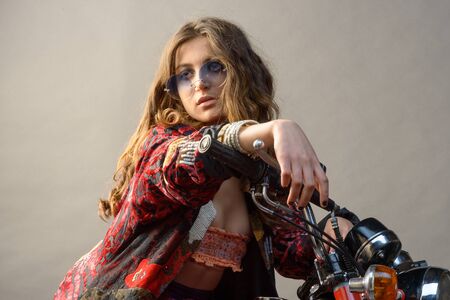 A sexy girl sit on a bike with hands on the handlebar long blonde hair and sunglassの写真素材