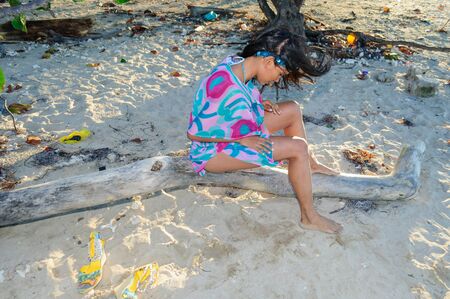 Beautiful and sexy girl posing at the beach in dominican republic sitting on a trunkの写真素材