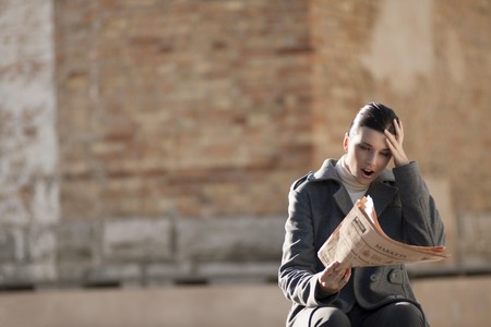 Young woman getting bad news from a financial newspaperの写真素材