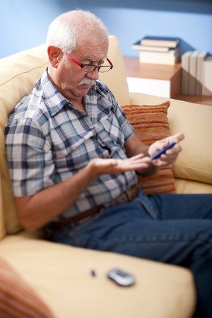 Senior man doing blood sugar test at homeの写真素材