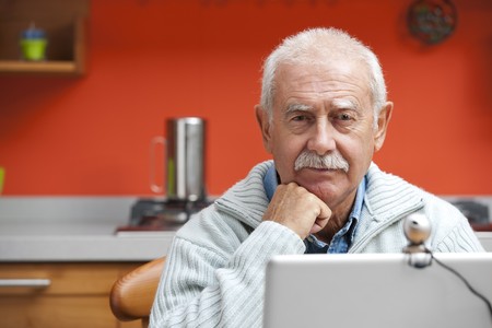 Senior man speaking through webcam in his kitchenの写真素材