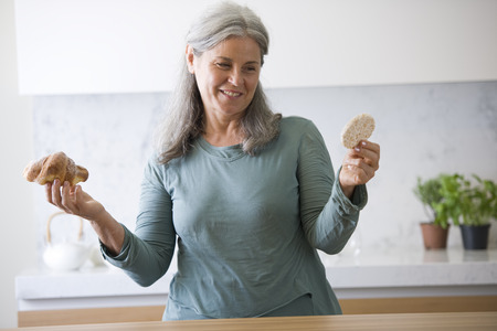 Senior woman choosing between rice snack and brioche