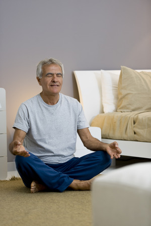 Senior man doing yoga/meditation in his bedroomの写真素材