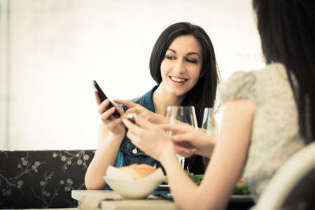 Female friends at the restaurant using mobile phoneの写真素材