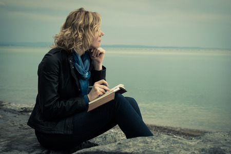 Woman writing her thoughts or poetry by the seaの写真素材