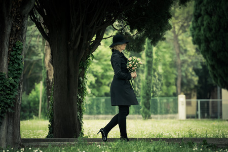 Woman walking in a cemetery holding flowersの写真素材