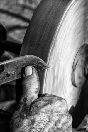 Sharpening a knife blade on a wet sandstone grinding wheelの写真素材