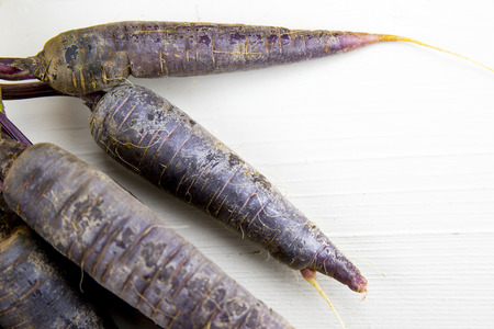 Bunch of heirloom purple carrots, over white and wooden background.の写真素材