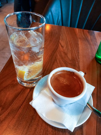 A cup of coffee and a glass containing water with ice cubes and a lemon wedgeの写真素材