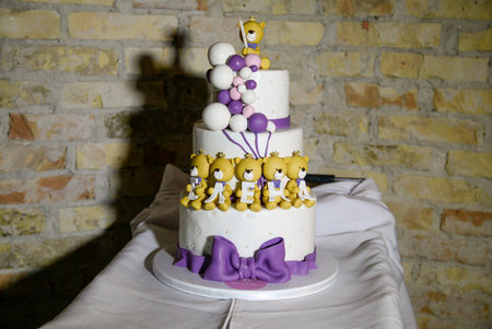 A three-tier white birthday cake decorated with yellow teddy bears holding letters with the female name written on it.の写真素材