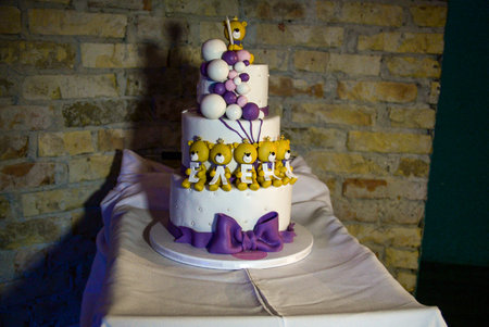 A three-tier white birthday cake decorated with yellow teddy bears holding Cyrillic letters.の写真素材