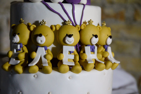 A three-tier white birthday cake decorated with yellow teddy bears holding letters with the female name written on it.の写真素材