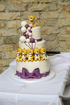 A three-tier white birthday cake decorated with yellow teddy bears holding letters with the female name Elena written on it.の写真素材