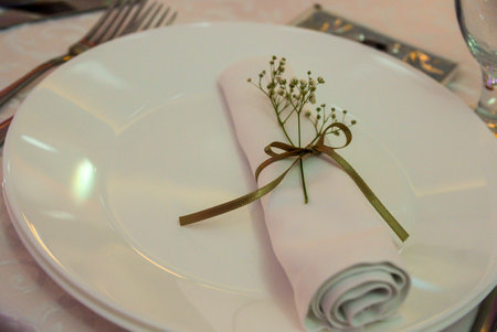 A white plate with a curled napkin tied with a gold ribbon and decorated with a sprig with white flowersの写真素材