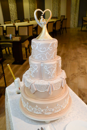 A four-tier pastel pink bridal cake decorated with oriental motifs drawn on fondant and a figure of the newlyweds in gold inside a gold heartの写真素材