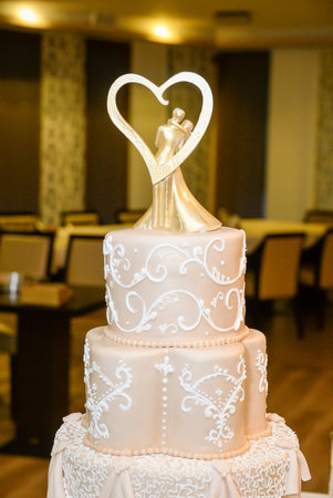A four-tier pastel pink bridal cake decorated with oriental motifs drawn on fondant and a figure of the newlyweds in gold inside a gold heartの写真素材