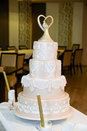 A four-tier pastel pink bridal cake decorated with oriental motifs drawn on fondant and a figure of the newlyweds in gold inside a gold heartの写真素材