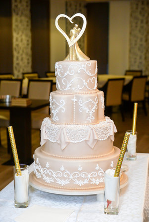 A four-tier pastel pink bridal cake decorated with oriental motifs drawn on fondant and a figure of the newlyweds in gold inside a gold heartの写真素材