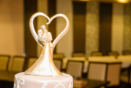 A four-tier pastel pink bridal cake decorated with oriental motifs drawn on fondant and a figure of the newlyweds in gold inside a gold heartの写真素材