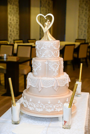 A four-tier pastel pink bridal cake decorated with oriental motifs drawn on fondant and a figure of the newlyweds in gold inside a gold heartの写真素材