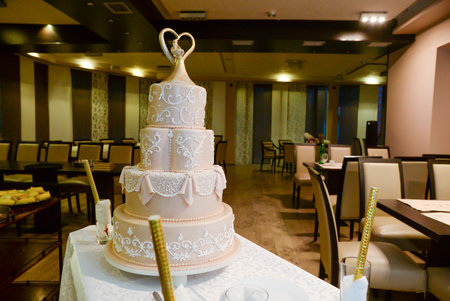 A four-tier pastel pink bridal cake decorated with oriental motifs drawn on fondant and a figure of the newlyweds in gold inside a gold heartの写真素材