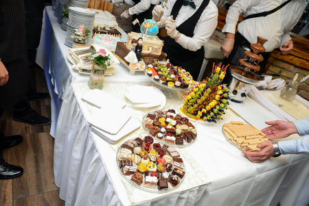 A serving table with a wedding cake, a chocolate fountain, fruit decorations and small cakes in various colors.の写真素材