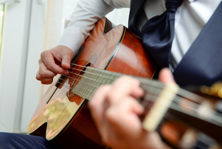 Close up of a man in a formal suit playing an acoustic guitar in a room. in the frame are his hands playing the guitarの写真素材