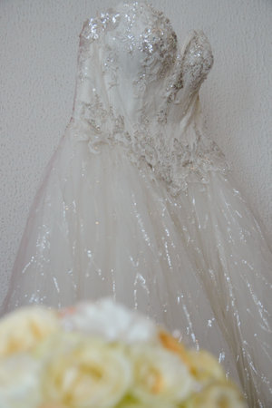 A white lace wedding dress in front of a white wall and in front of it is a bouquet of beautiful flowersの写真素材