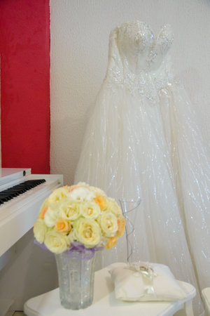 A white lace wedding dress in front of a white wall and in front of it is a bouquet of beautiful flowersの写真素材
