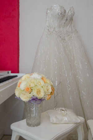 A white lace wedding dress in front of a white wall and in front of it is a bouquet of beautiful flowersの写真素材