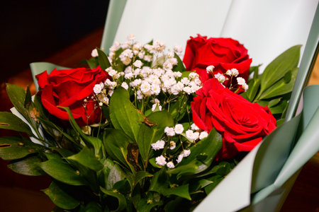 A bouquet of three roses in light green decorative paper with a red bow as an ideal gift for a loved oneの写真素材