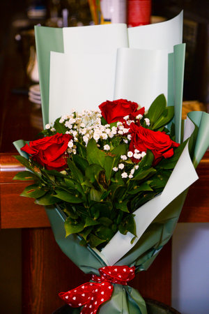 A bouquet of three roses in light green decorative paper with a red bow as an ideal gift for a loved oneの写真素材