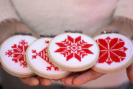 Woman holding hand made cross stitch folk Christmas decoration ornament embroidery on plywood. Nordic snowflakes.の写真素材