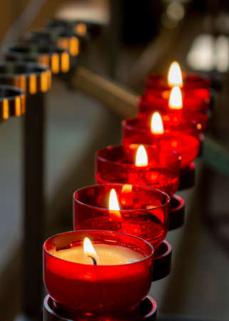 Burning red prayer candles inside a catholic church on a candle rack. Selective focus.の写真素材