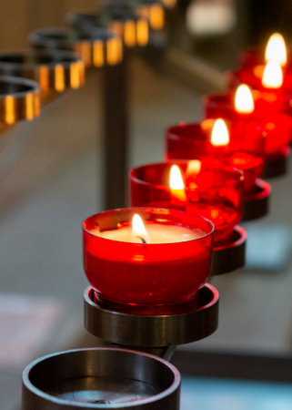 Burning red prayer candles inside a catholic church on a candle rack. Selective focus.の写真素材