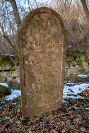 Old ancient abandoned jewish cemetery in the forest in the winter. Aged tombstones or gravestones in the graveyard.の写真素材