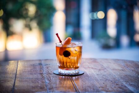 you can see a rum old fashioned on ice cocktail on a wooden table the color of which is orange transparent with a blurred backgroundの写真素材