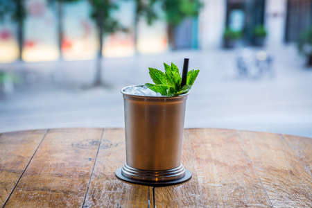 in the middle of the picture you can see a cocktail which is served in a metal cup with ice and straw. the mug is on a wooden table and the background is blurredの写真素材