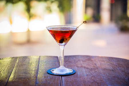 In the picture you can see a cocktail decorated with a cherry, the glass stands on a wooden table and the background is blurredの写真素材