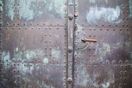 You can see an old bluish metal wall whose surface looks old and washed out with rivets and a door...