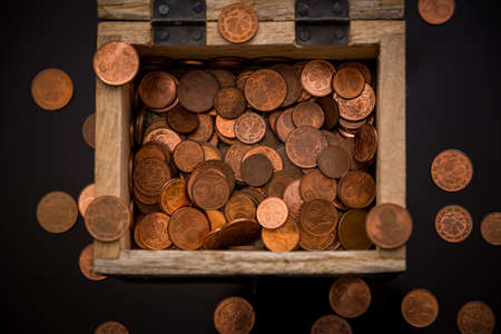 In the picture you can see a small wooden treasure chest in which you can see many different coins that are also scattered aroundの写真素材